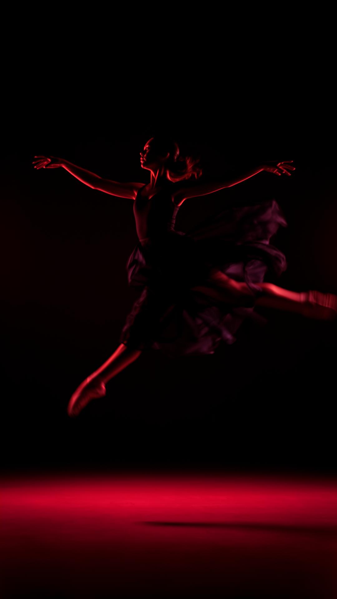 Dancer mid-leap under crimson stage light