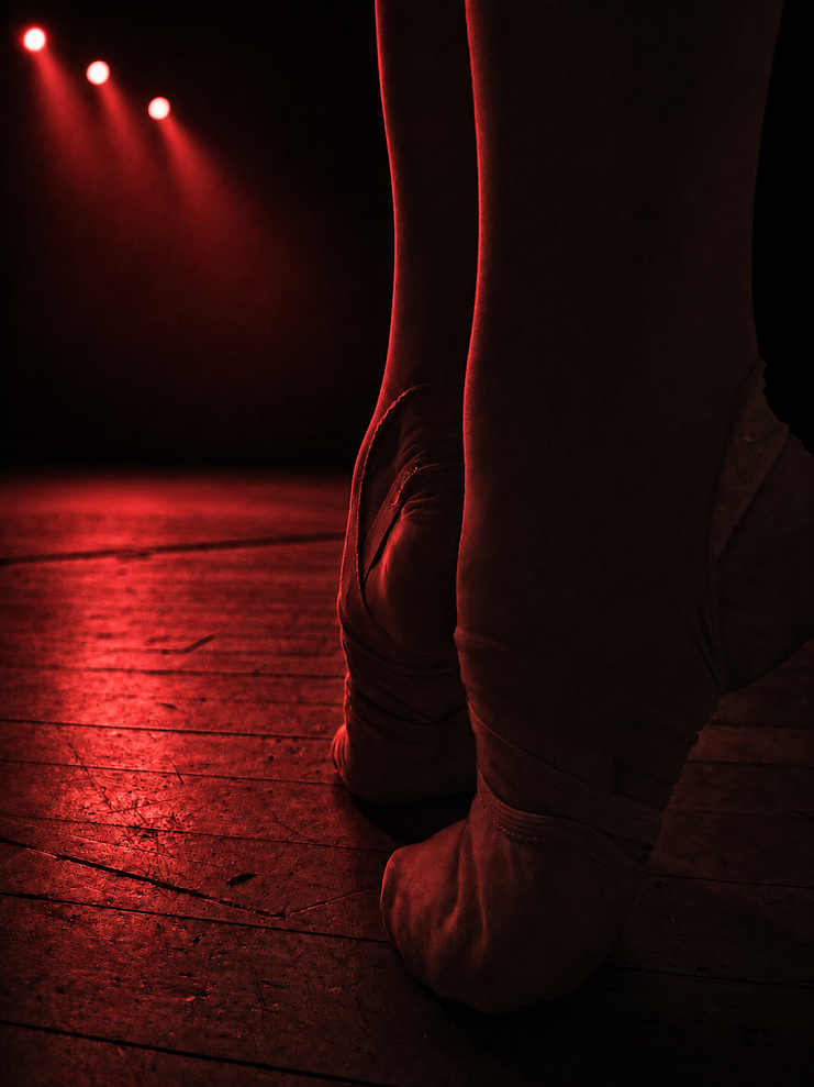 Dancer mid-leap under crimson stage light